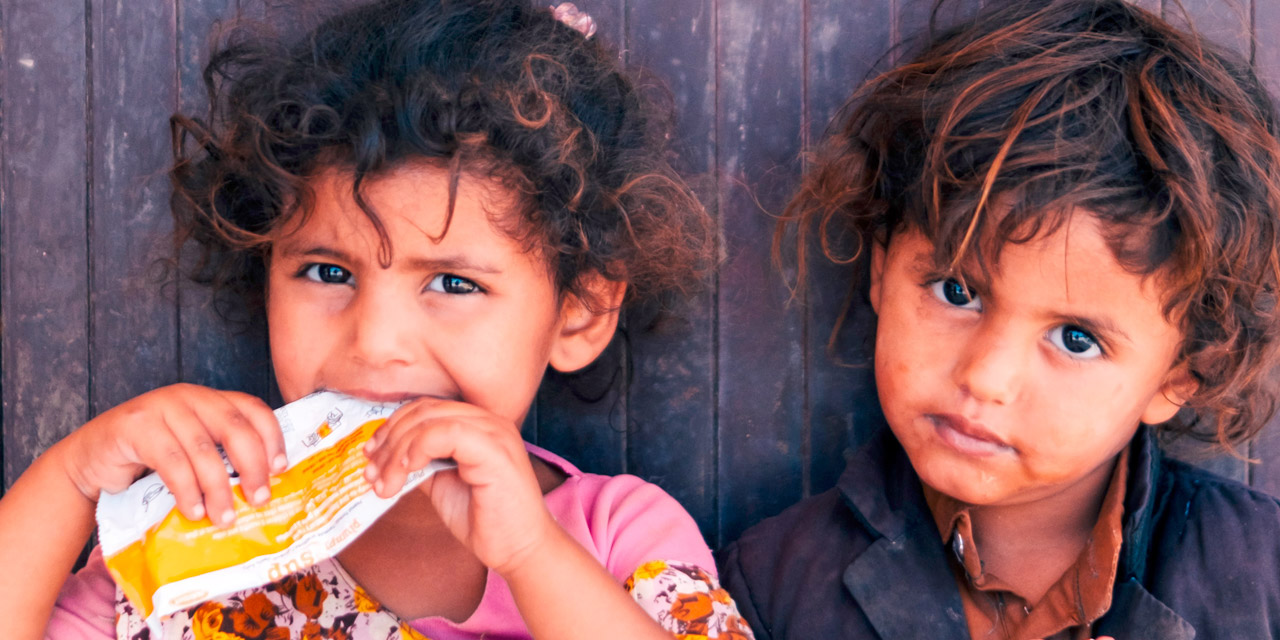 Photo showing siblings Ittefa and Ramsey enjoying a packet of supplementary food outside a WFP-supported nutrition centre in Marib, Yemen.